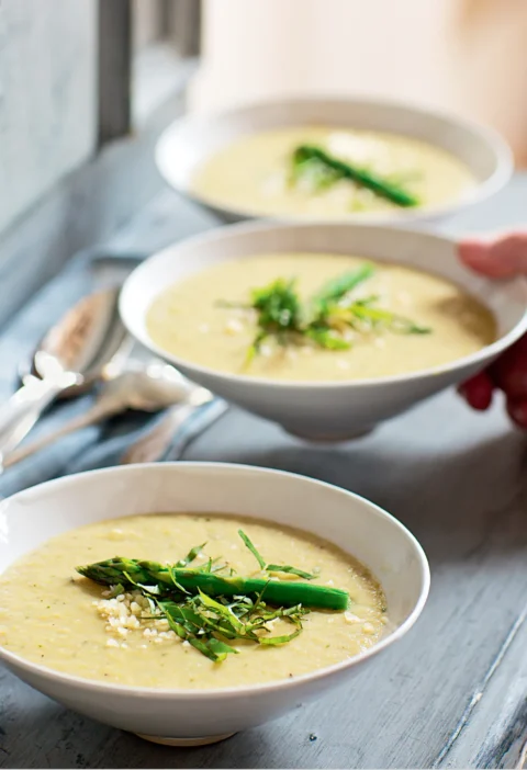Ina Garten asparagus and fennel soup in white bowls topped with a blanched asparagus tip, julienned basil and grated Parmesan
