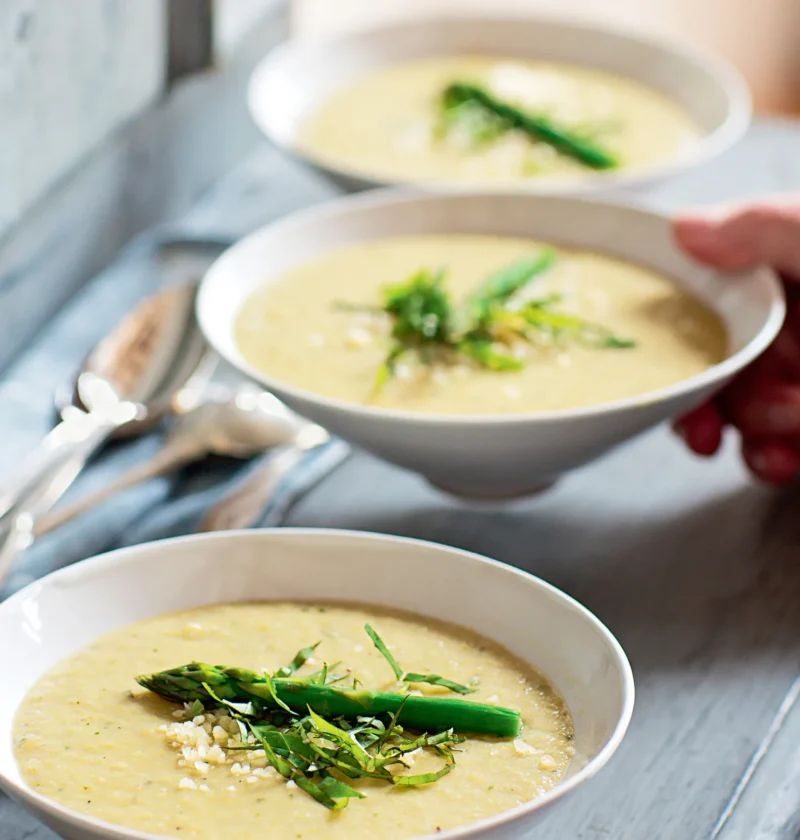 Ina Garten asparagus and fennel soup in white bowls topped with a blanched asparagus tip, julienned basil and grated Parmesan