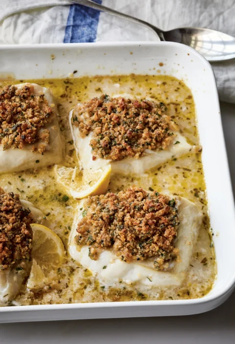 Ina Garten baked cod with garlic & herb Ritz crumbs in a white baking dish with lemon slices and pan juices