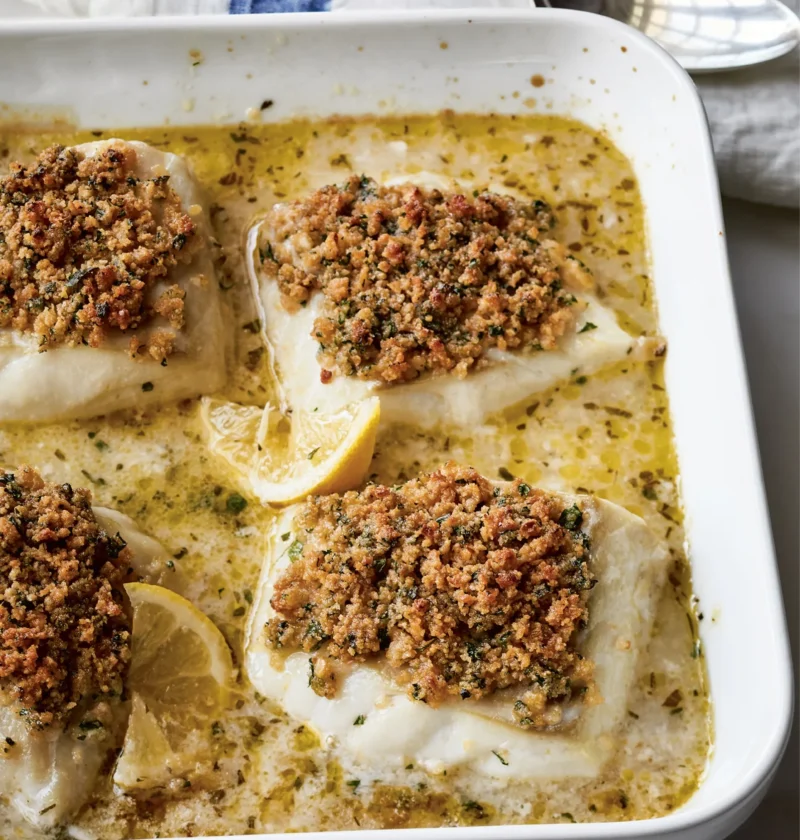 Ina Garten baked cod with garlic & herb Ritz crumbs in a white baking dish with lemon slices and pan juices