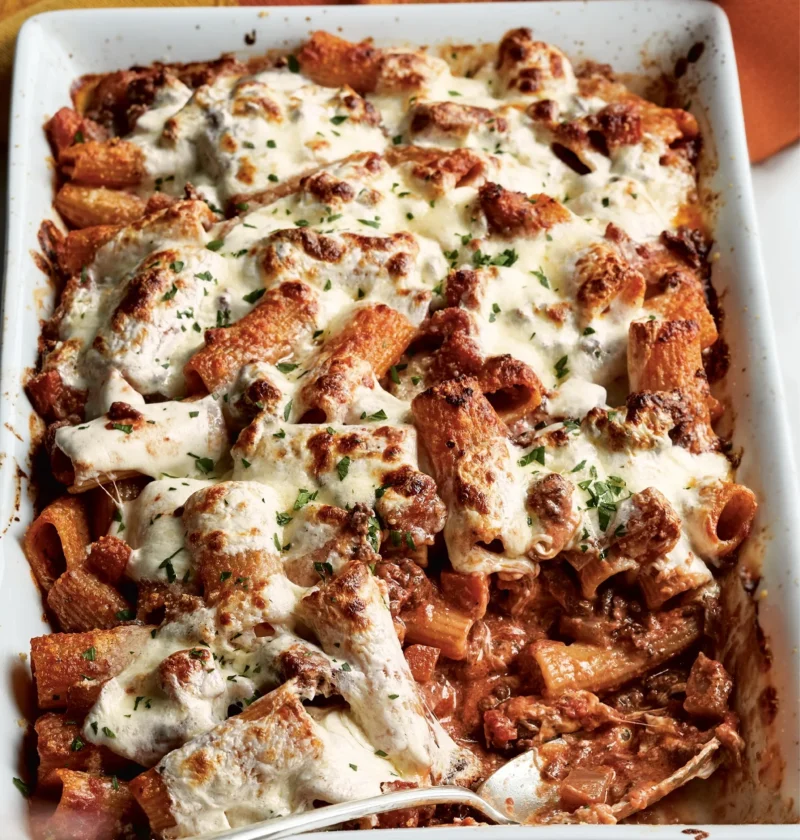 Ina Garten baked rigatoni with lamb ragù topped with melted mozzarella in a white baking dish with a serving spoon