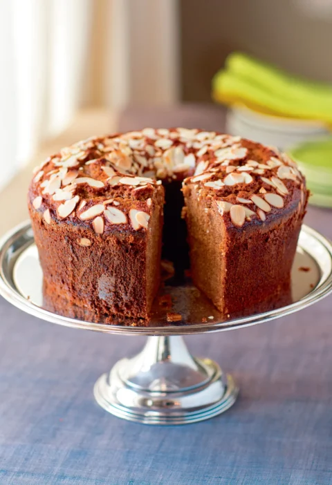 Ina Garten bourbon honey cake topped with sliced almonds on a silver cake stand with a slice cut out