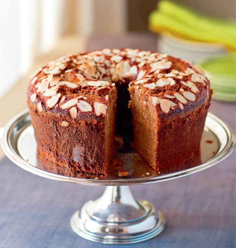 Ina Garten bourbon honey cake topped with sliced almonds on a silver cake stand with a slice cut out
