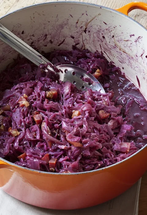 Ina Garten braised red cabbage with pancetta in an orange Dutch oven with a slotted spoon
