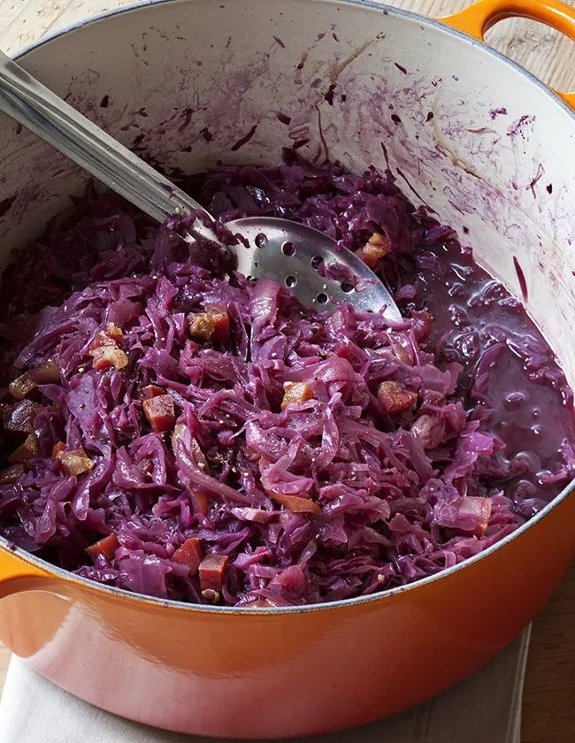 Ina Garten braised red cabbage with pancetta in an orange Dutch oven with a slotted spoon