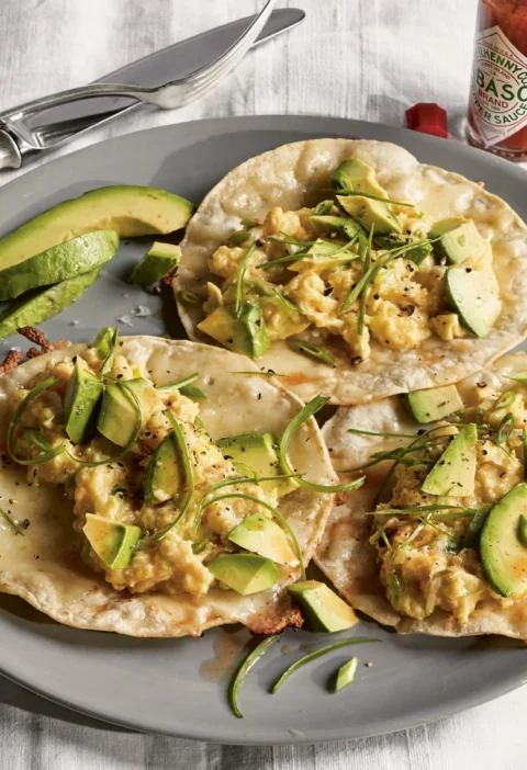 Ina Garten breakfast tacos with scrambled eggs, sliced avocado and scallion greens on toasted corn tortillas on a gray plate