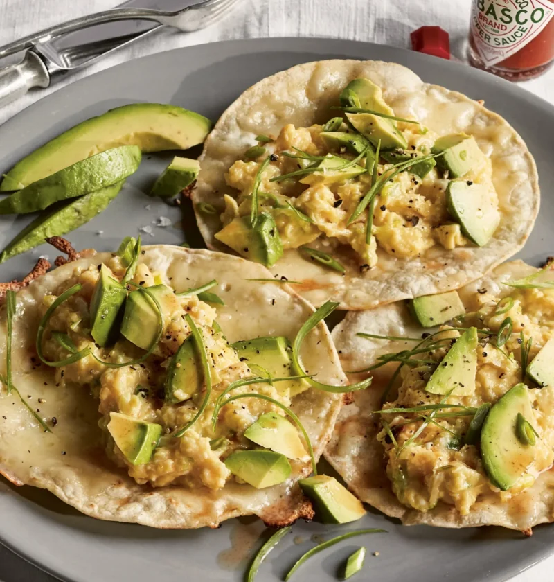 Ina Garten breakfast tacos with scrambled eggs, sliced avocado and scallion greens on toasted corn tortillas on a gray plate