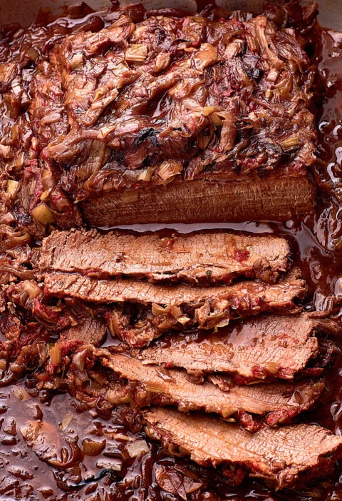 Ina Garten brisket with onions and leeks, sliced thick and covered in a glossy red wine onion sauce in a roasting pan