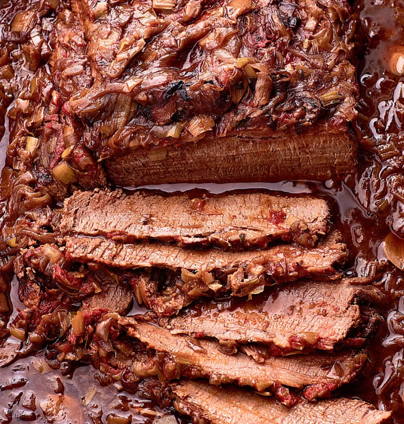 Ina Garten brisket with onions and leeks, sliced thick and covered in a glossy red wine onion sauce in a roasting pan