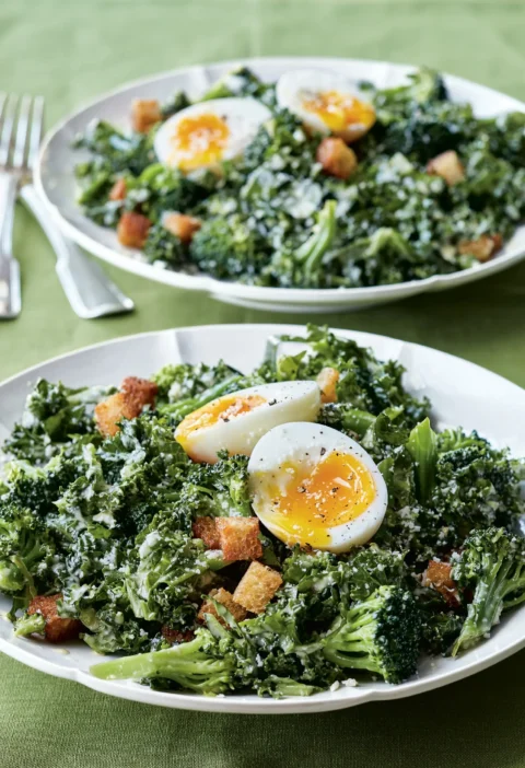 Ina Garten broccoli & kale salad with halved soft-boiled eggs, croutons and Caesar dressing on two white plates