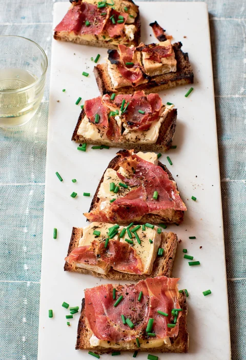 Ina Garten camembert and prosciutto tartines on a white marble board topped with crispy prosciutto and chopped chives