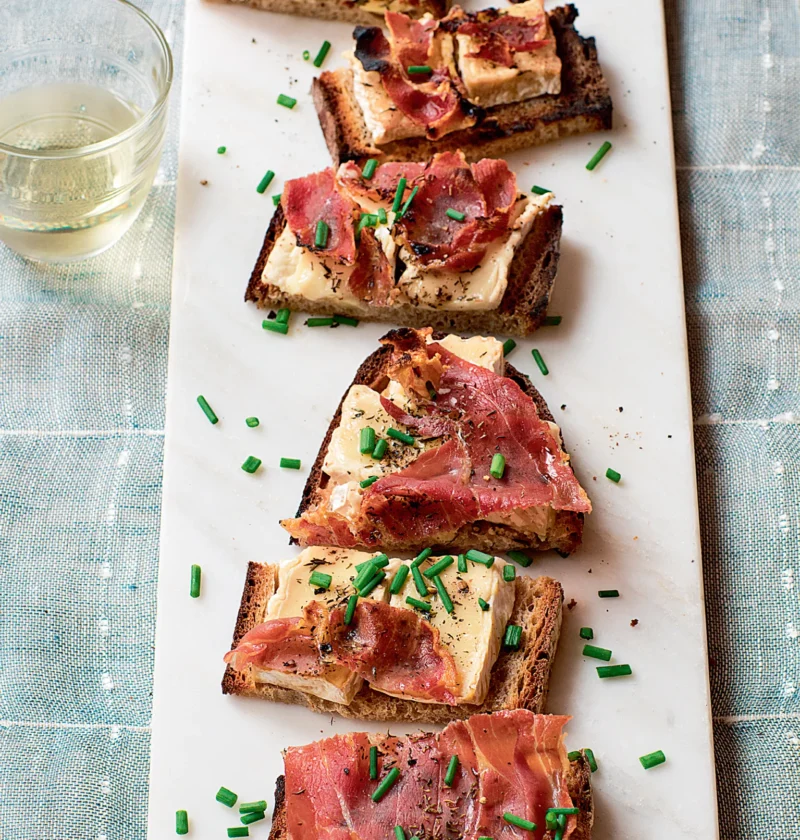 Ina Garten camembert and prosciutto tartines on a white marble board topped with crispy prosciutto and chopped chives