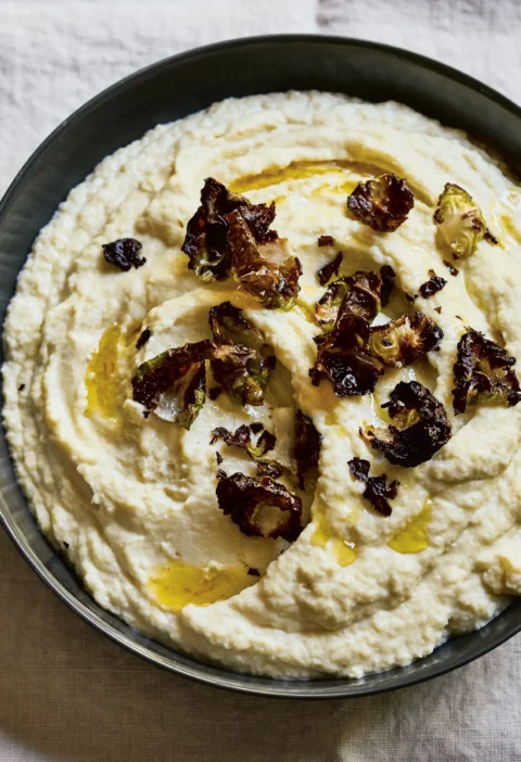 Ina Garten celery root & cauliflower purée in a dark bowl topped with crispy roasted Brussels sprout leaves and a drizzle of olive oil