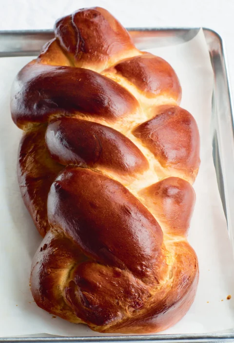 Ina Garten challah with saffron, a glossy golden braided egg bread on parchment paper on a sheet pan