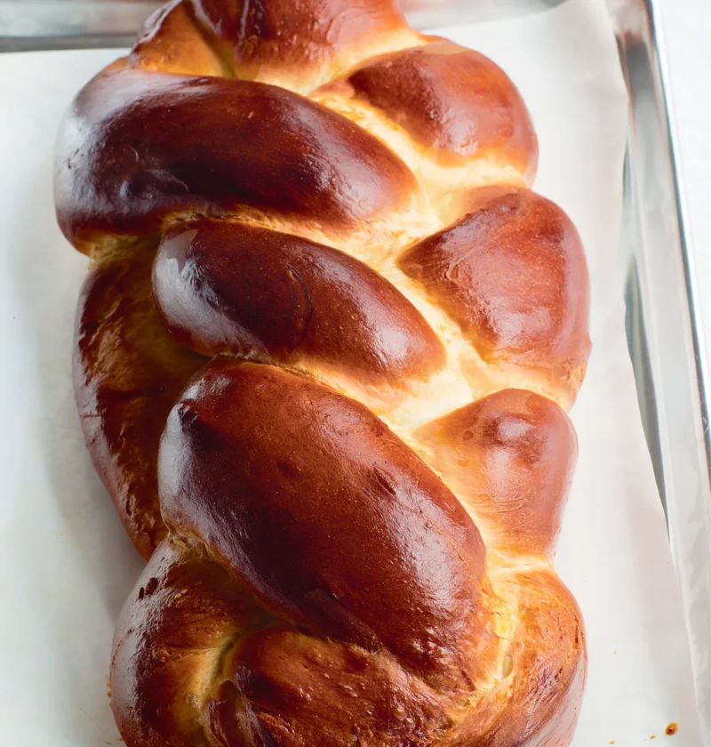 Ina Garten challah with saffron, a glossy golden braided egg bread on parchment paper on a sheet pan