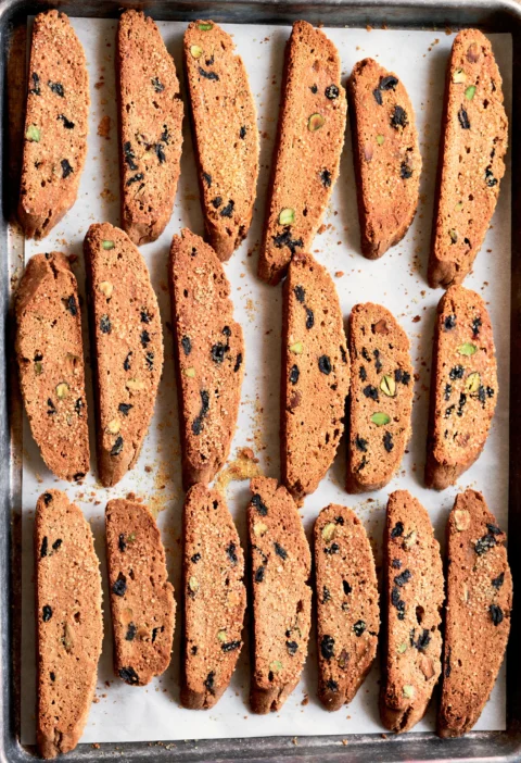 Ina Garten cherry pistachio biscotti sliced and arranged on a parchment-lined sheet pan with visible dried cherries and pistachios