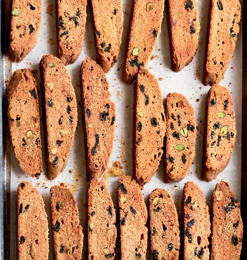 Ina Garten cherry pistachio biscotti sliced and arranged on a parchment-lined sheet pan with visible dried cherries and pistachios