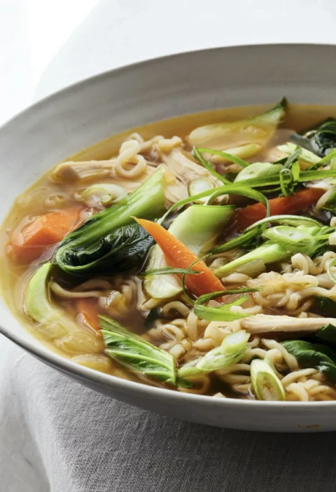 Ina Garten chicken ramen-noodle soup with shredded chicken, carrots, baby bok choy and scallions in a white bowl