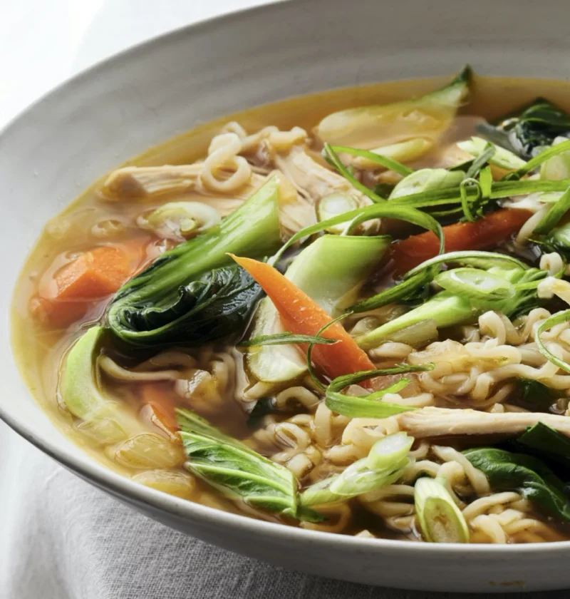 Ina Garten chicken ramen-noodle soup with shredded chicken, carrots, baby bok choy and scallions in a white bowl