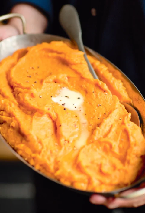 Ina Garten chipotle smashed sweet potatoes in an oval baking dish with a pat of melting butter and black pepper