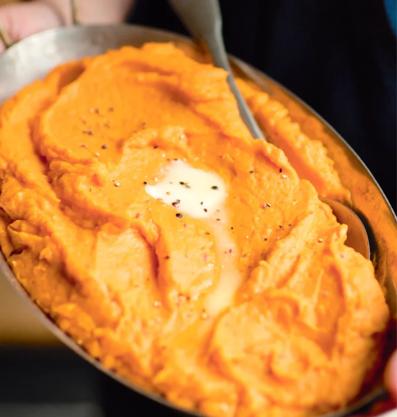 Ina Garten chipotle smashed sweet potatoes in an oval baking dish with a pat of melting butter and black pepper