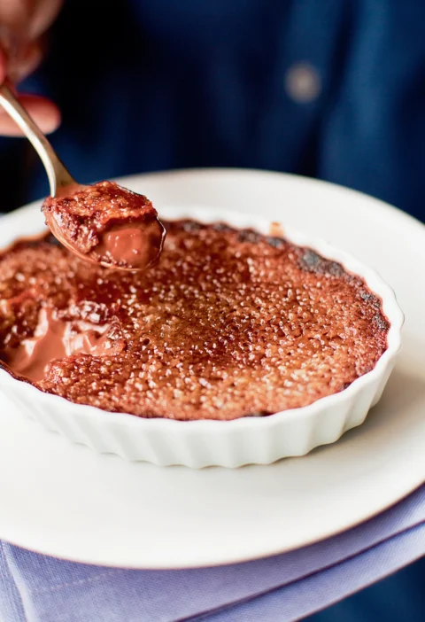 Ina Garten chocolate crème brûlée in a white fluted ramekin with a caramelized sugar top and a spoon lifting out a bite of creamy chocolate custard