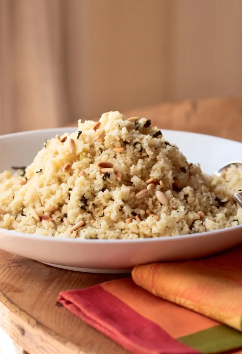 Ina Garten couscous with pine nuts and mint piled in a white bowl with toasted pine nuts and fresh mint