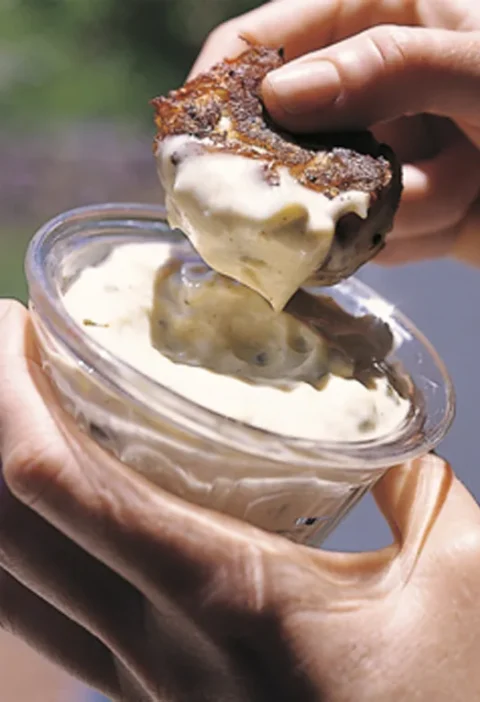 Ina Garten crab cake dipped in creamy remoulade sauce held over a small glass bowl