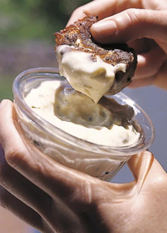 Ina Garten crab cake dipped in creamy remoulade sauce held over a small glass bowl