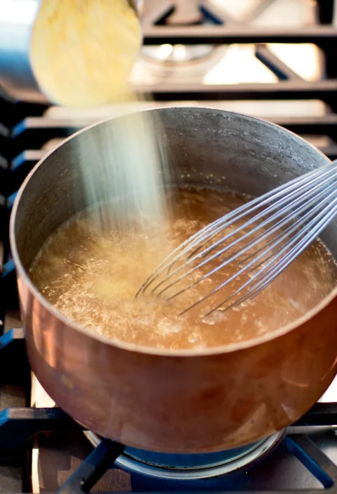 Ina Garten creamy parmesan polenta cornmeal being whisked into simmering chicken stock in a copper saucepan on the stove