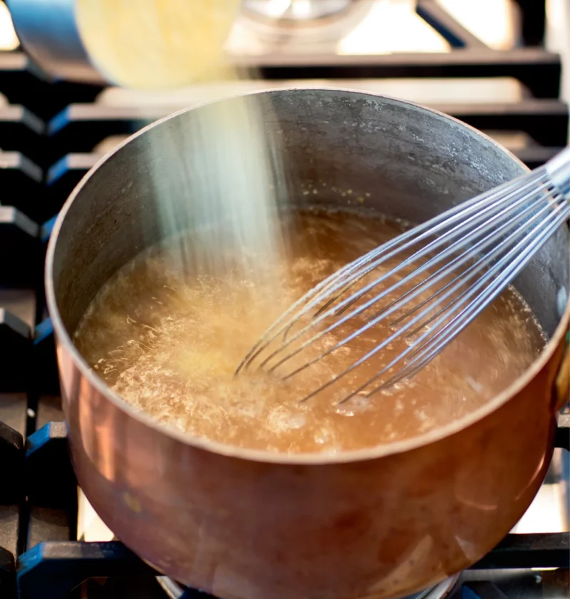 Ina Garten creamy parmesan polenta cornmeal being whisked into simmering chicken stock in a copper saucepan on the stove