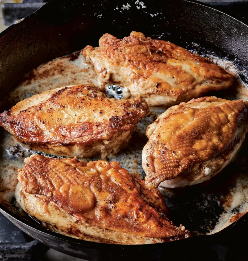 Ina Garten crispy chicken with golden skin-on breasts browning in butter in a cast-iron skillet