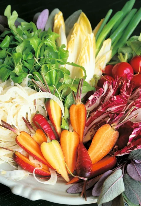 Ina Garten crudité platter with baby carrots, radicchio, endive, fennel, radishes, arugula and scallions arranged on a white platter