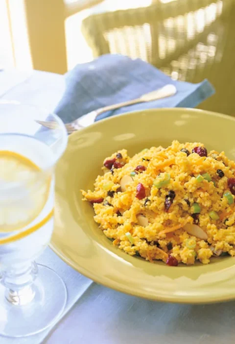 Ina Garten curried couscous with currants, almonds and scallions in a yellow bowl next to a glass of lemon water