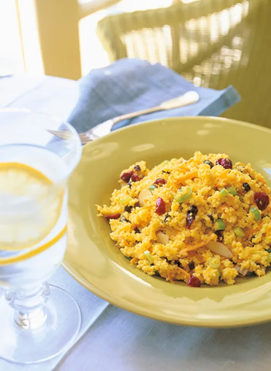 Ina Garten curried couscous with currants, almonds and scallions in a yellow bowl next to a glass of lemon water