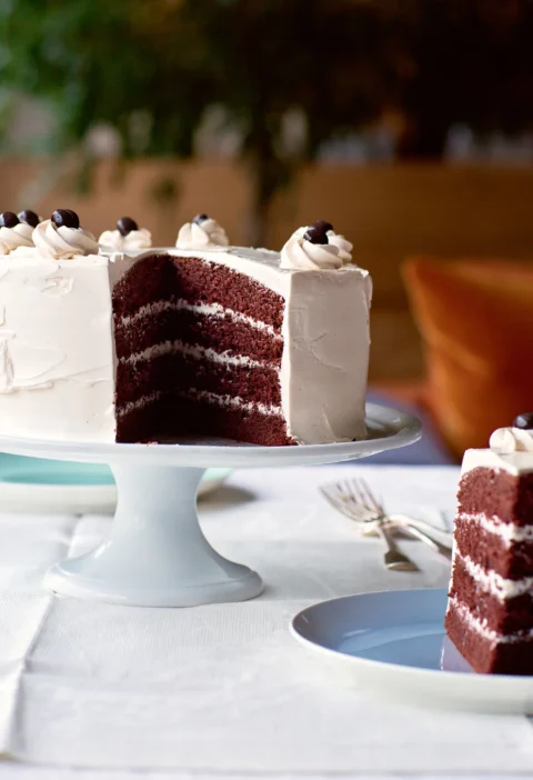 Ina Garten devil's food cake with coffee meringue buttercream cut to show four chocolate layers, topped with chocolate espresso beans