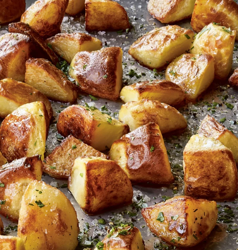 Ina Garten Emily's English roasted potatoes, golden crispy chunks sprinkled with sea salt and parsley on a sheet pan