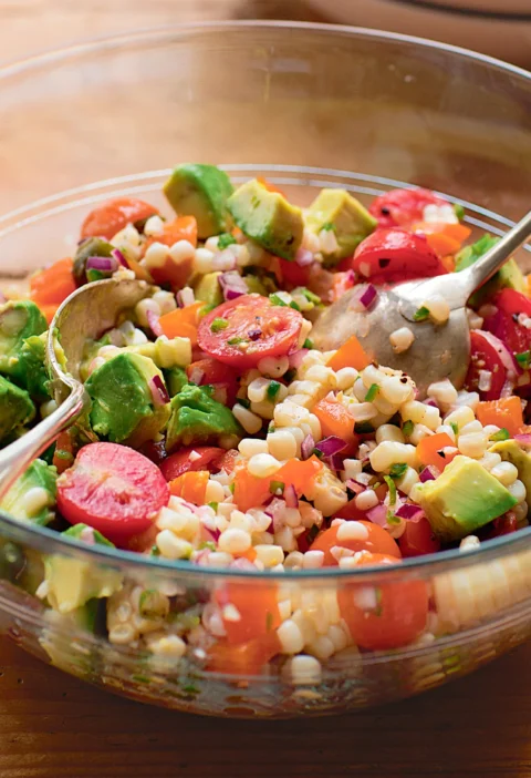 Ina Garten fiesta corn and avocado salad with corn kernels, cherry tomatoes, diced avocado and red onion in a glass bowl
