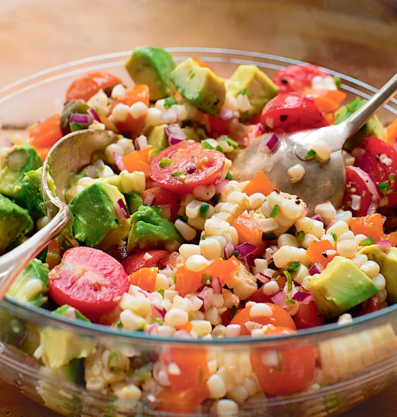 Ina Garten fiesta corn and avocado salad with corn kernels, cherry tomatoes, diced avocado and red onion in a glass bowl