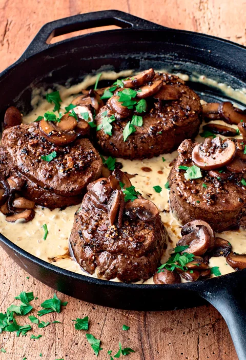Ina Garten filet mignon with mustard and mushrooms in a cast iron skillet with creamy mustard sauce and fresh parsley