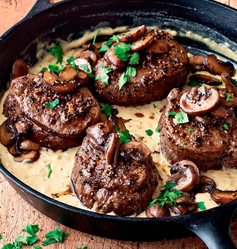 Ina Garten filet mignon with mustard and mushrooms in a cast iron skillet with creamy mustard sauce and fresh parsley