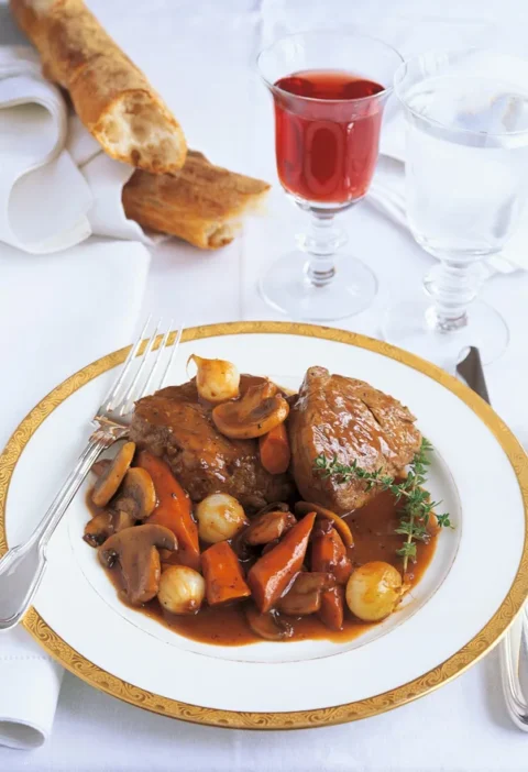 Ina Garten filet of beef bourguignon on a gold-rimmed plate with carrots, pearl onions and mushrooms in red wine sauce