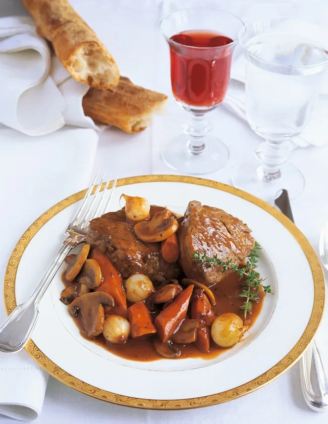 Ina Garten filet of beef bourguignon on a gold-rimmed plate with carrots, pearl onions and mushrooms in red wine sauce