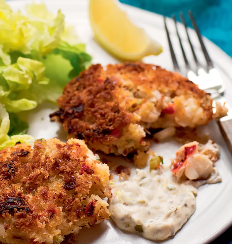 Ina Garten fish and lobster cakes golden brown with panko crust served with rémoulade sauce, lettuce and a lemon wedge