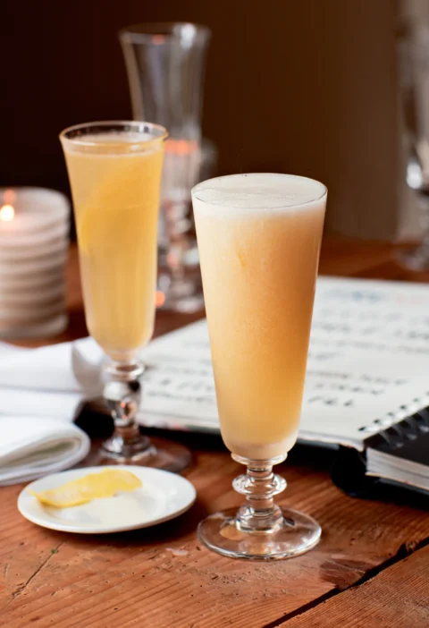 Ina Garten French 75 cocktails in two tall Champagne flutes with a strip of lemon zest on a small plate beside them