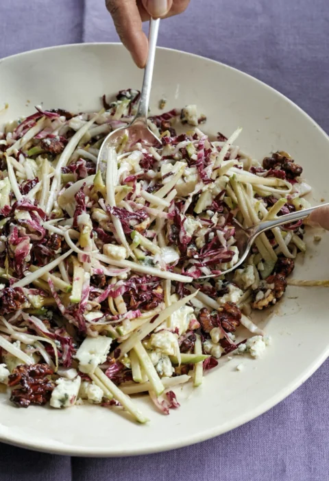 Ina Garten French bistro salad with shredded radicchio, endive, apple matchsticks, Roquefort and caramelized walnuts being tossed in a white bowl