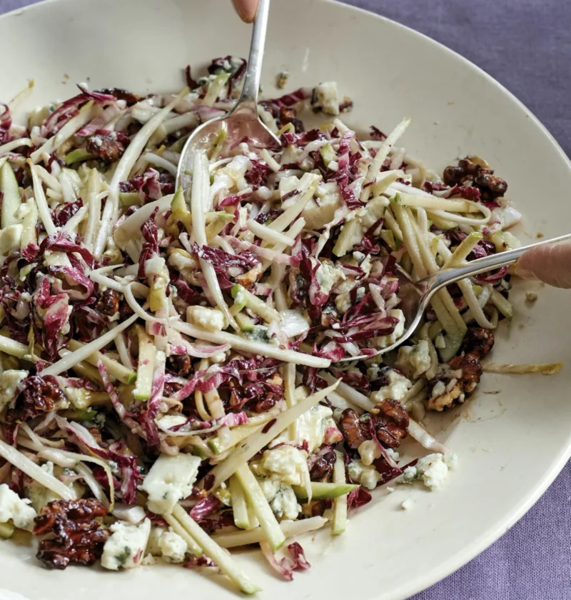 Ina Garten French bistro salad with shredded radicchio, endive, apple matchsticks, Roquefort and caramelized walnuts being tossed in a white bowl