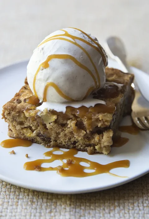 Ina Garten fresh apple spice cake square topped with vanilla ice cream and caramel sauce on a white plate