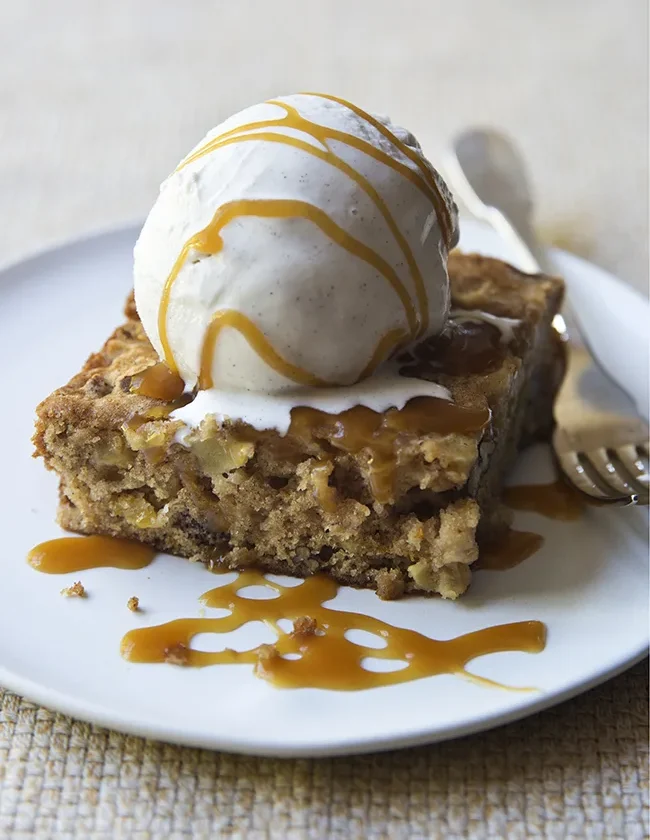 Ina Garten fresh apple spice cake square topped with vanilla ice cream and caramel sauce on a white plate