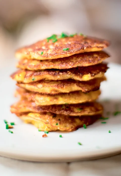 Stack of golden Ina Garten fresh corn pancakes topped with minced chives on a white plate